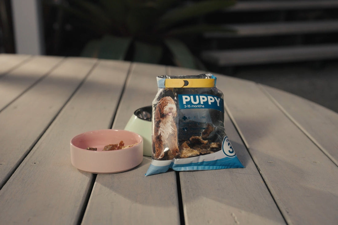 A bag of pet treats next to a dog bowl on a deck.