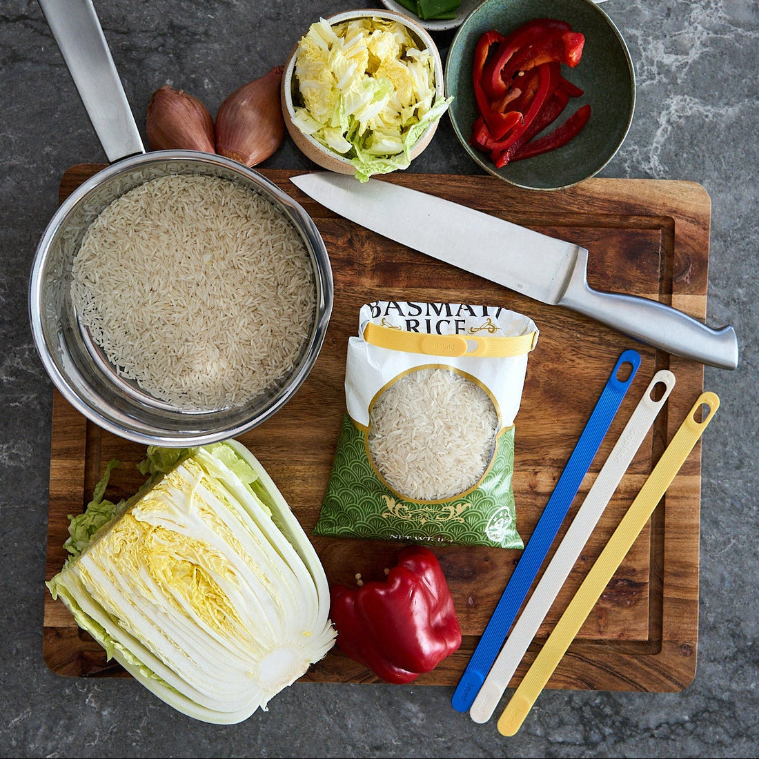 a bag of rice that has been looplocked on a cutting board, with various food items and cooking utensils around it.