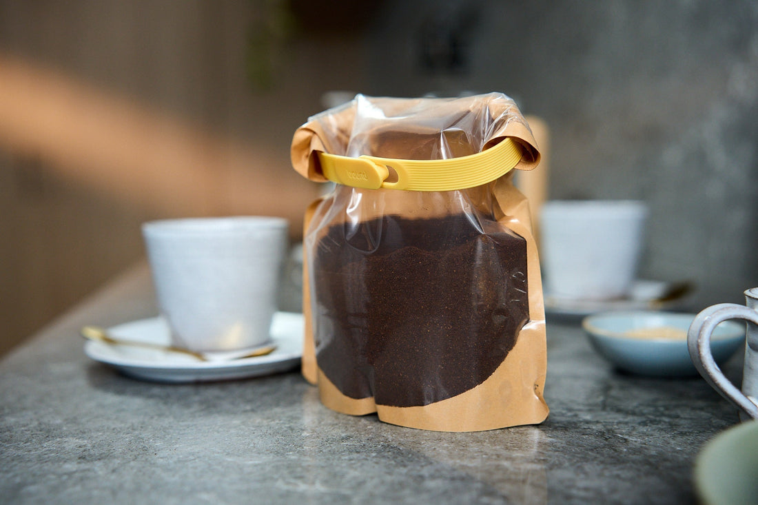 A bag of coffee sealed with a Looplock next to a coffee cup on a kitchen counter.