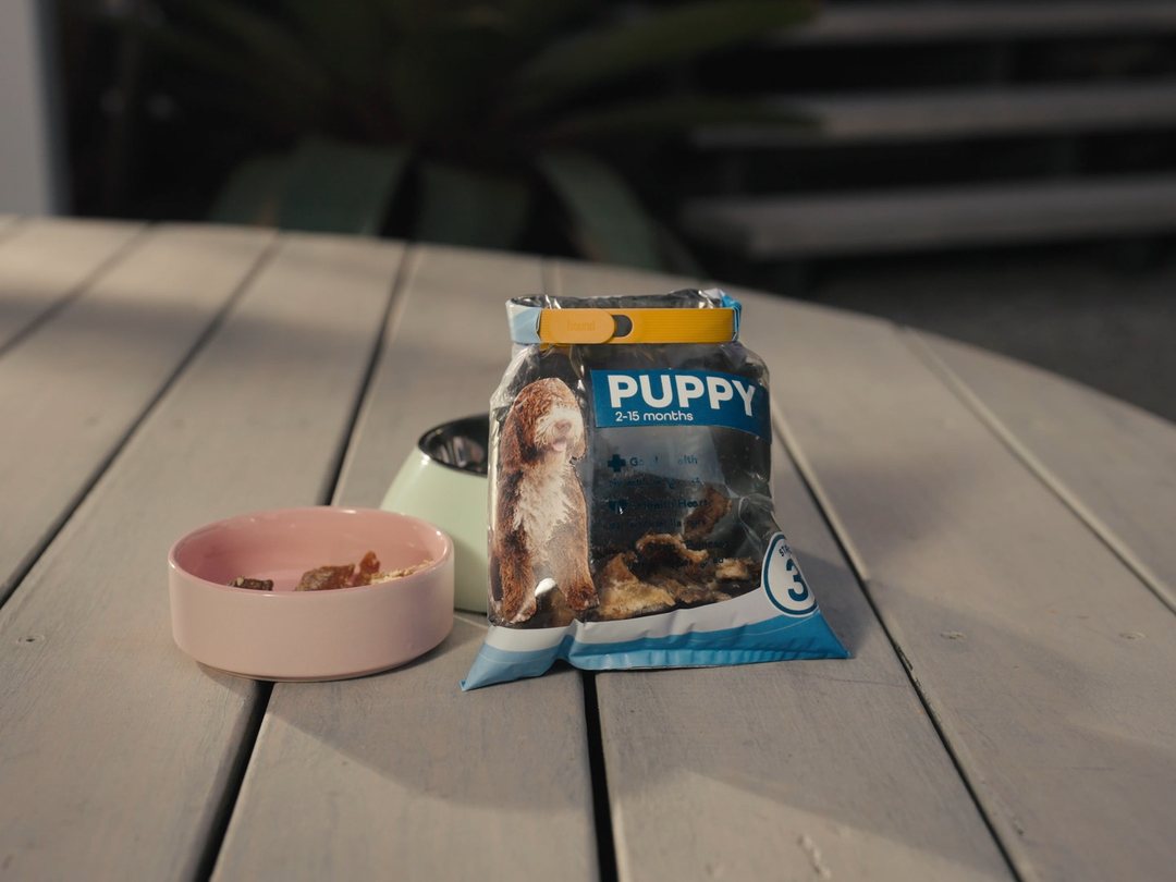 A bag of puppy treats on an outdoor table next to a dog bowl, sealed with a Mango Looplock